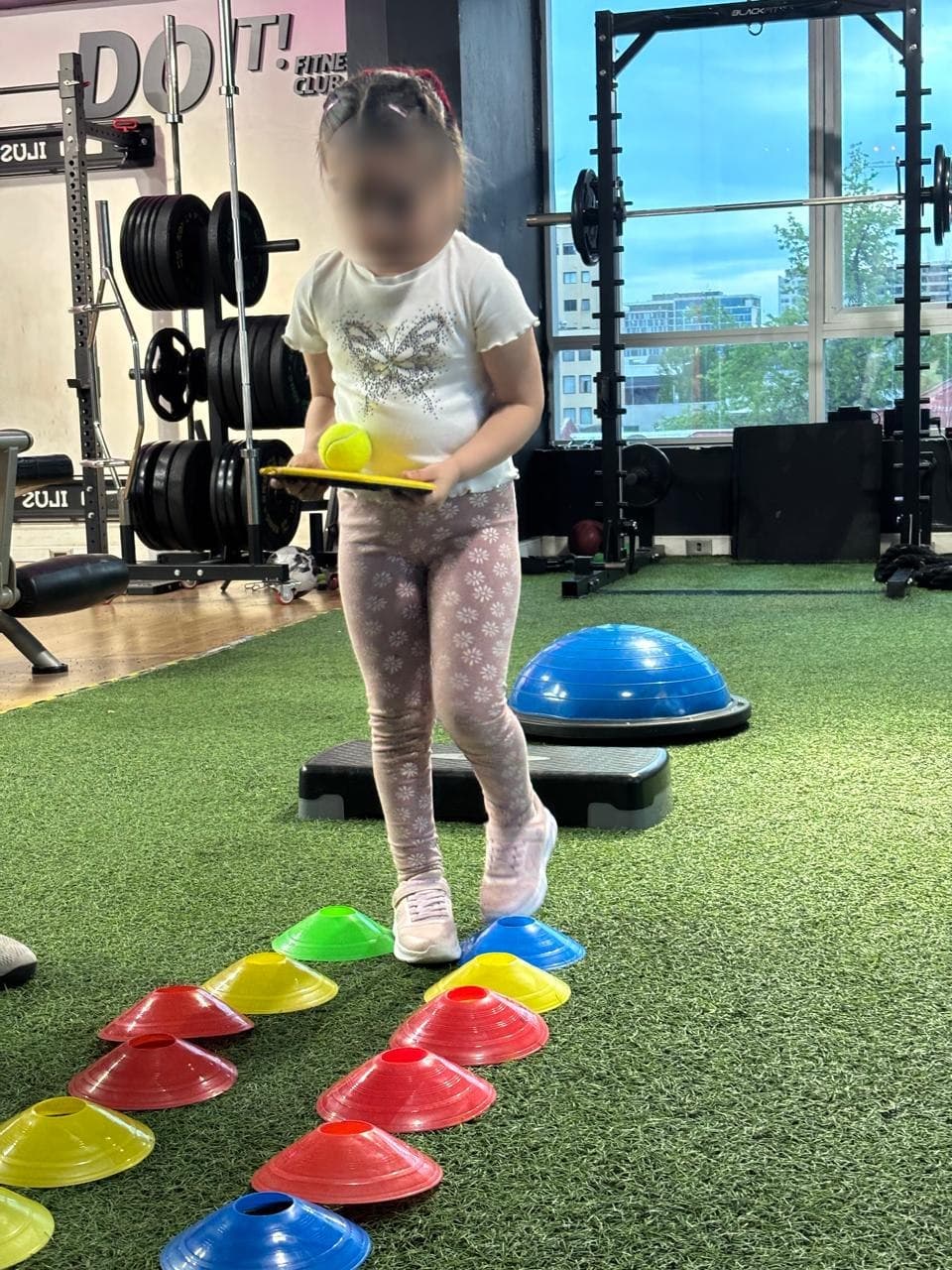 Niña recorriendo un circuito de equilibrio con conos de colores mientras sostiene una pelota sobre una paleta
